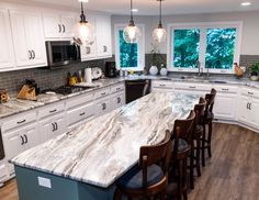 a large kitchen with marble counter tops and white cabinets, along with dark wood flooring