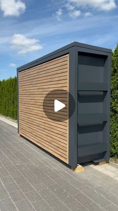 a large wooden box sitting on the side of a road next to a green hedge