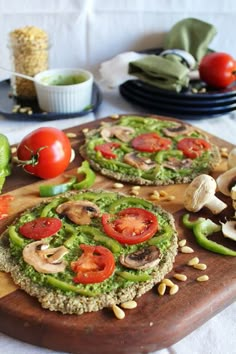 two pizzas with mushrooms, tomatoes and green peppers on a cutting board next to other food items