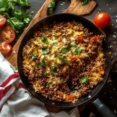 a skillet filled with rice and vegetables on top of a wooden cutting board next to tomatoes