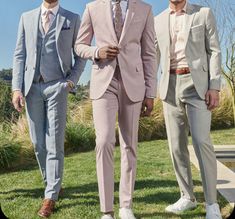 three men in suits are standing on the grass outside, one is wearing white shoes