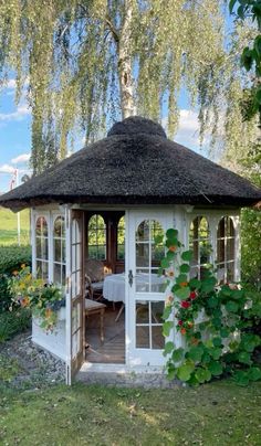 a white gazebo sitting in the middle of a lush green field next to a tree