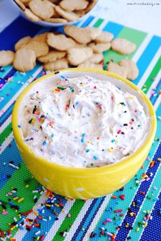 a yellow bowl filled with white frosting and sprinkles next to cookies