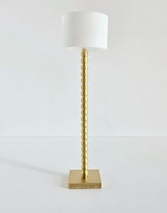 a lamp that is on top of a white surface with a gold base and a white lampshade