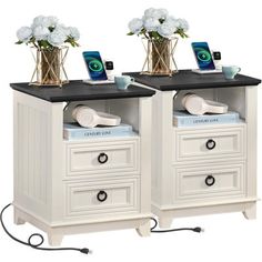 two white nightstands with black top and drawers on each side, one has flowers in vases