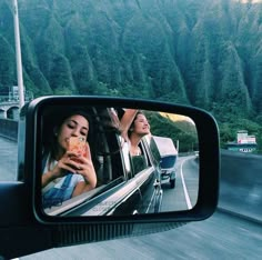 two women taking pictures in the rear view mirror of a car as it drives down a mountain road