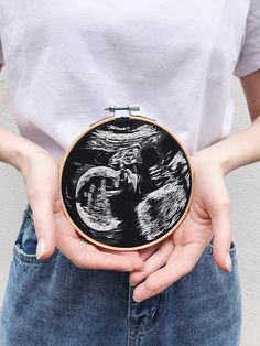 a woman holding a black and white cross - stitched art piece in her hands