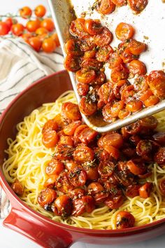 someone scooping tomatoes over spaghetti in a red bowl