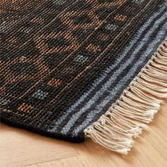 a rug with fringes on top of it and a wooden floor in the background