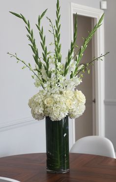 a vase filled with white flowers sitting on top of a wooden dining room table in front of a doorway