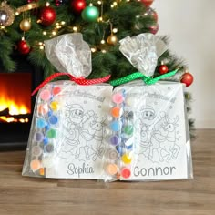 two bags filled with candy sitting next to a christmas tree in front of a fireplace