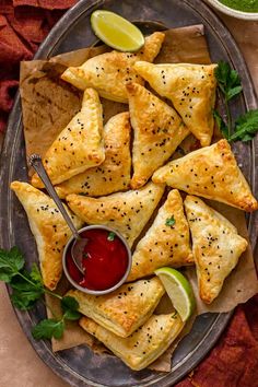 several pastries on a plate with dipping sauce and garnished lime wedges