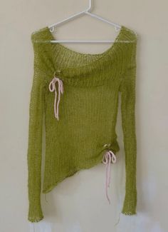 a green sweater hanging on a hanger next to a white wall with a pink tie