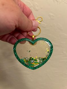 a hand holding a heart shaped ornament with green and gold flecks