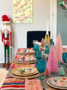 the table is set for christmas dinner with colorful plates and silverware, candy - cane trees, and nutcrackers