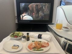 an airplane tray with food and drinks in front of a television screen on the plane