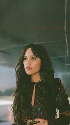 a woman with long dark hair is looking at the camera and she has her hands on her hips