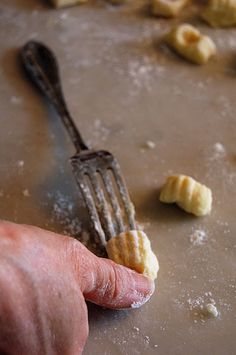 a person holding a fork with some food on top of it and small pieces of bread in the background