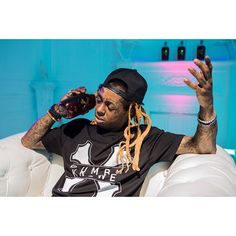 a man with dreadlocks sitting on a white couch drinking from a beer bottle