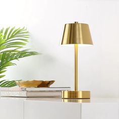 a gold lamp sitting on top of a white table next to a potted plant