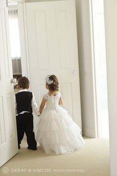 two young children dressed in formal wear are looking at each other as they stand in front of an open door