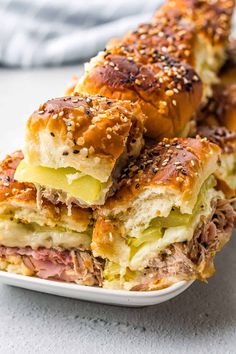 three sandwiches stacked on top of each other in a white plate with sesame seeds and cheese