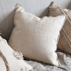 three pillows sitting on top of a white couch next to each other with tassels