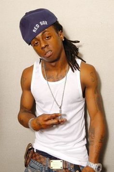 a man with dreadlocks wearing a white tank top and blue jeans holding a cell phone