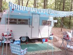 a camper parked in the woods next to some chairs and tables with flags on them