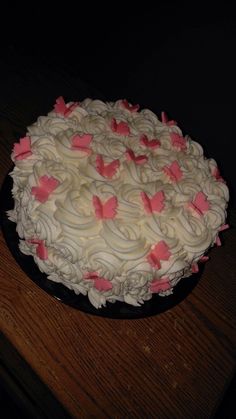 a cake with white frosting and pink bows on it sitting on a wooden table