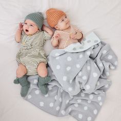 two babies laying on top of each other next to a white sheet covered in grey and white polka dots