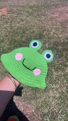 a child's hand wearing a green crocheted frog hat with pink eyes