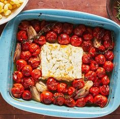 a blue casserole dish filled with tomatoes and other food on a wooden table