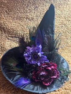 a hat with feathers and flowers in it on a carpeted floor, next to a pair of scissors