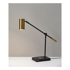 a black and gold desk lamp on a white table with a gray wall in the background