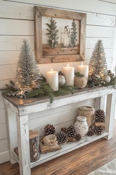 a mantle with candles and pine cones on it in front of a framed picture, surrounded by other christmas decorations