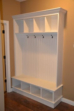 a white bench sitting in the middle of a room next to a wall mounted coat rack