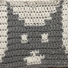 a gray and white crocheted cat pillow on top of a wooden table