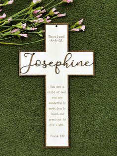 a cross with flowers on the ground and a bible verse written in wood above it