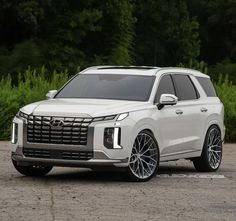 a white suv parked on top of a parking lot next to some grass and trees