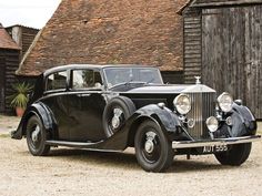 an old black car parked in front of a barn