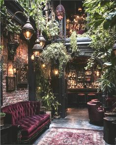 a living room filled with furniture and lots of greenery on the walls, along with hanging lights