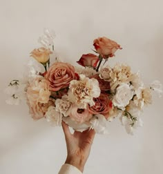 a hand holding a bouquet of flowers in front of a white wall with no one around it