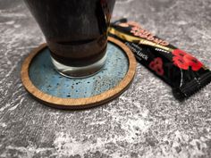 a chocolate bar next to a glass of dark liquid on a gray table with a wooden coaster