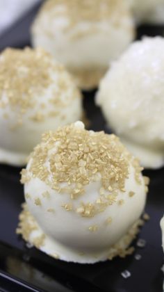 some white desserts with gold sprinkles are on a black plate