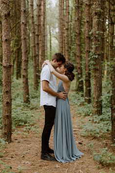 a man and woman standing in the middle of a forest hugging each other with their arms around each other