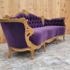 a purple couch sitting on top of a stone floor next to a wooden paneled wall