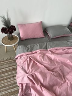 a bed with pink and grey sheets in a room next to a small table on the floor