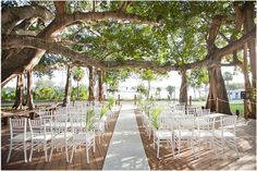 an outdoor ceremony setup with white chairs and trees