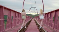 two women are walking across a pink bridge